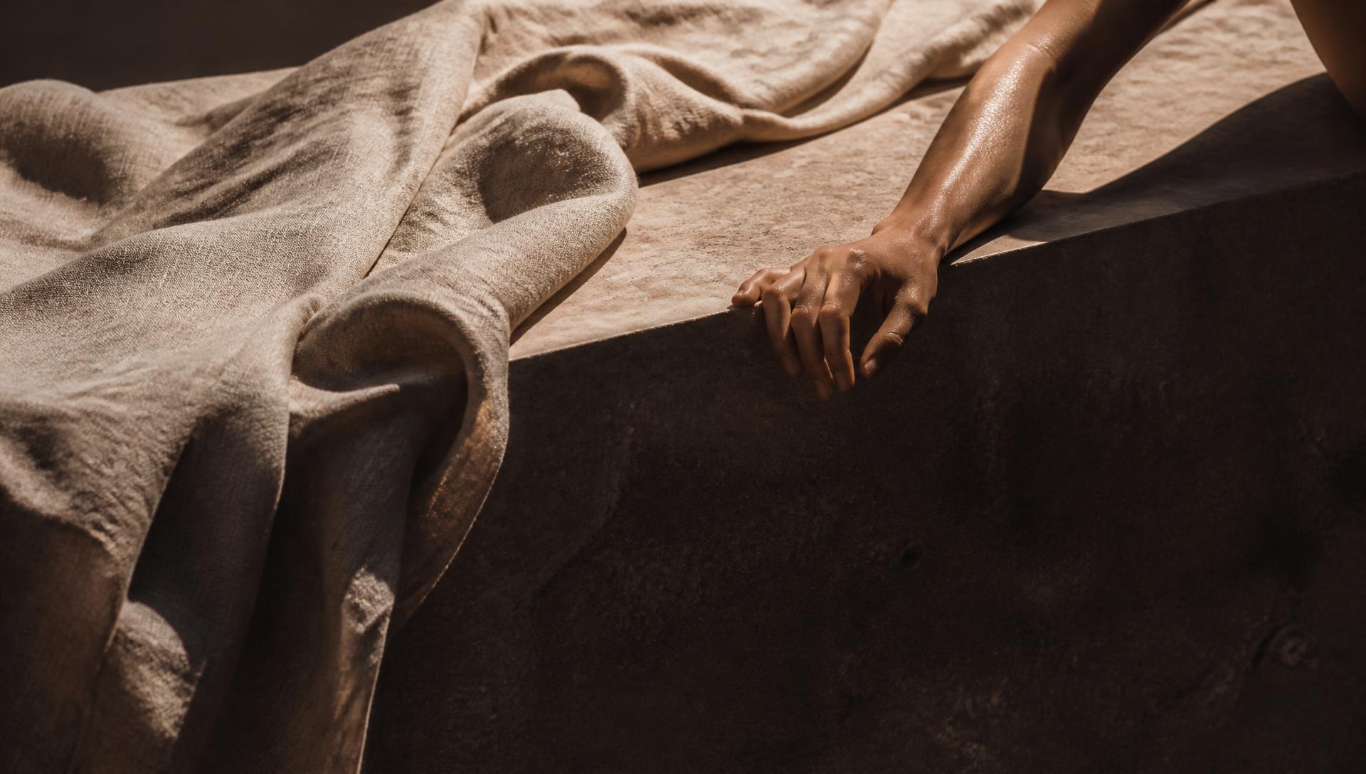 Linen drapery on a sunlit stone ledge with a resting hand